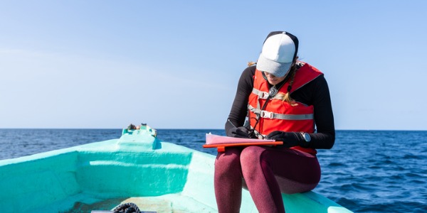 A marine biologist writing down data sitting on a boat.