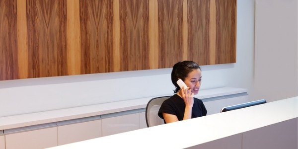 A receptionist sitting behind the desk and speaking on the phone.