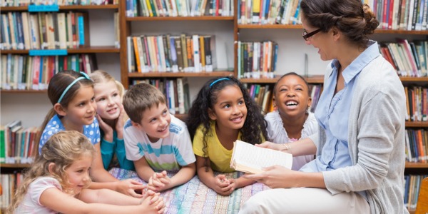 A school librarian talking to young students in the library.