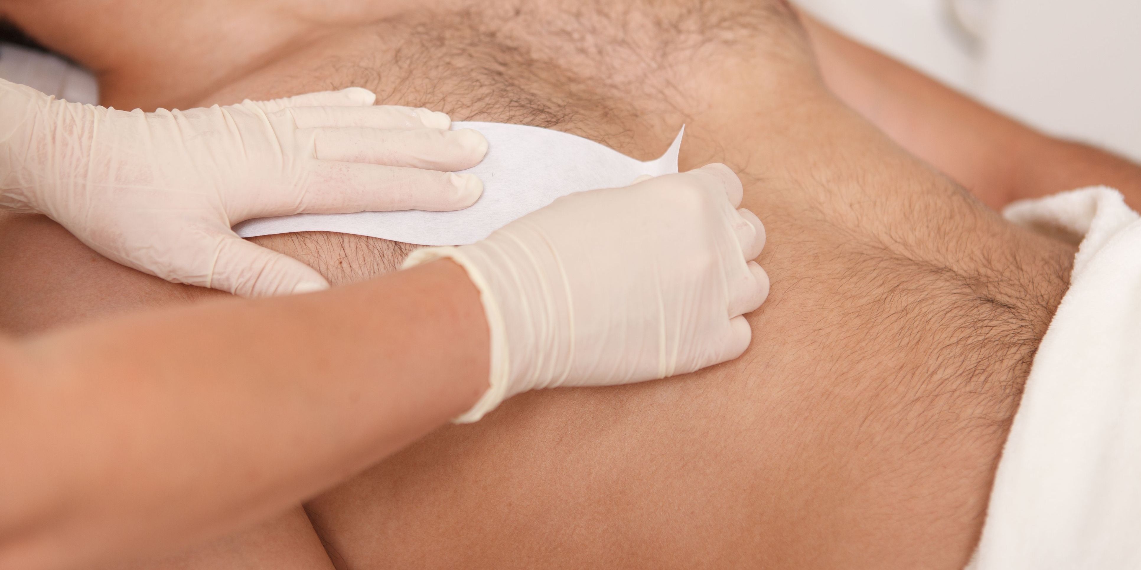 A hair removal specialist waxing a man's chest.